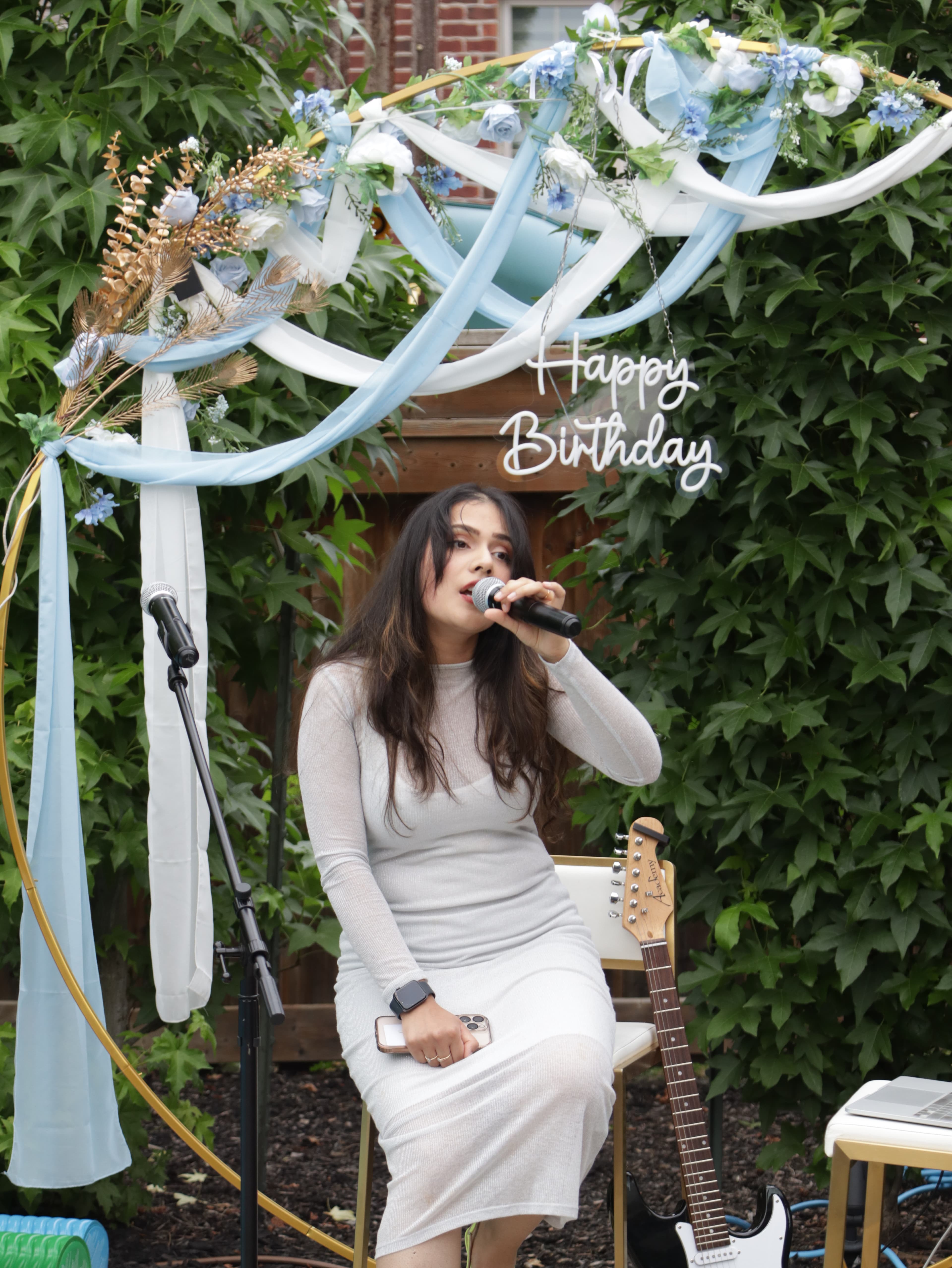 Woman singing into a microphone under a floral arch
